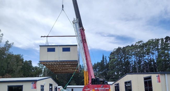 Crane in centre of temporary buildings lifting another off a truck into position